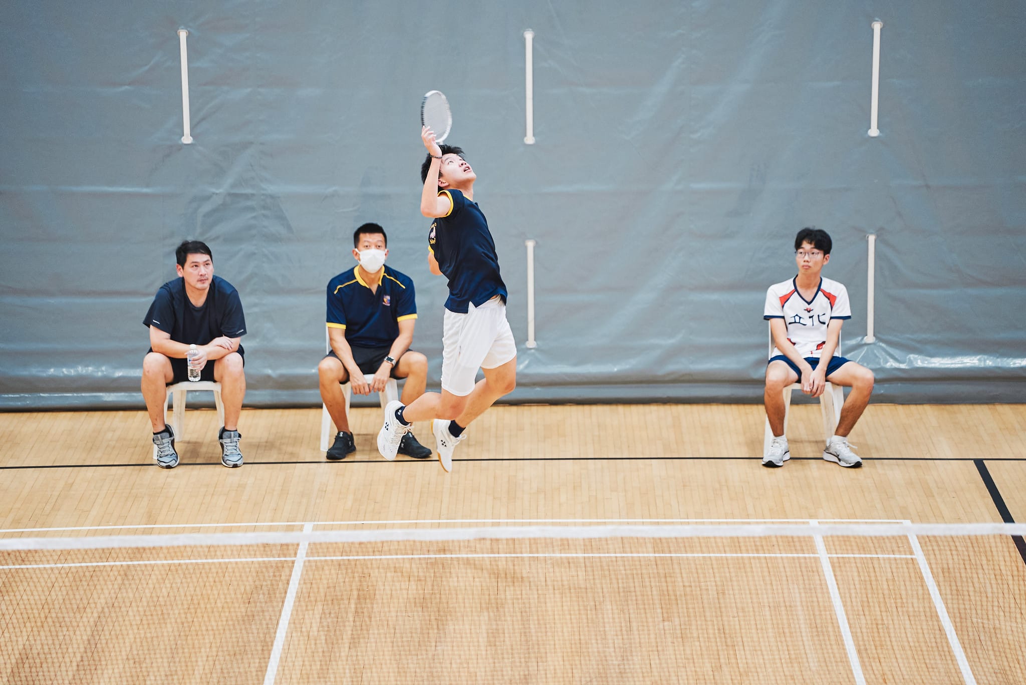 A player mid-jump to perform a move with coaches watching from the sideline in the background.